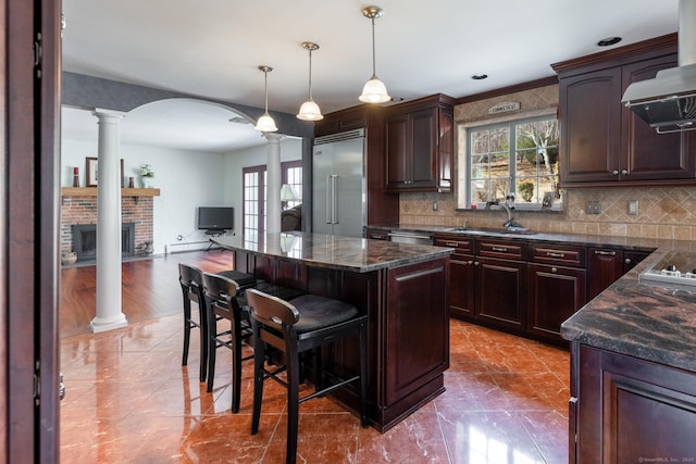 kitchen featuring decorative columns, stainless steel built in refrigerator, a sink, a kitchen island, and a kitchen bar