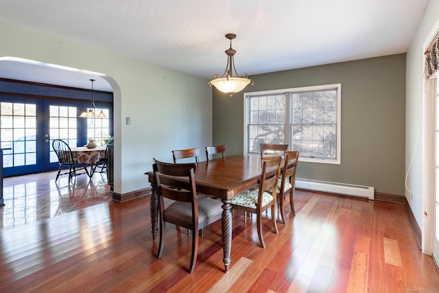 dining room with wood finished floors, arched walkways, baseboards, and baseboard heating