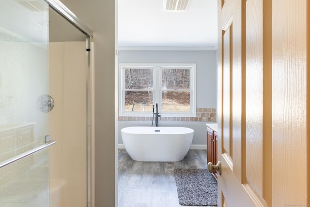 bathroom with wood finished floors, visible vents, ornamental molding, a freestanding bath, and a shower stall