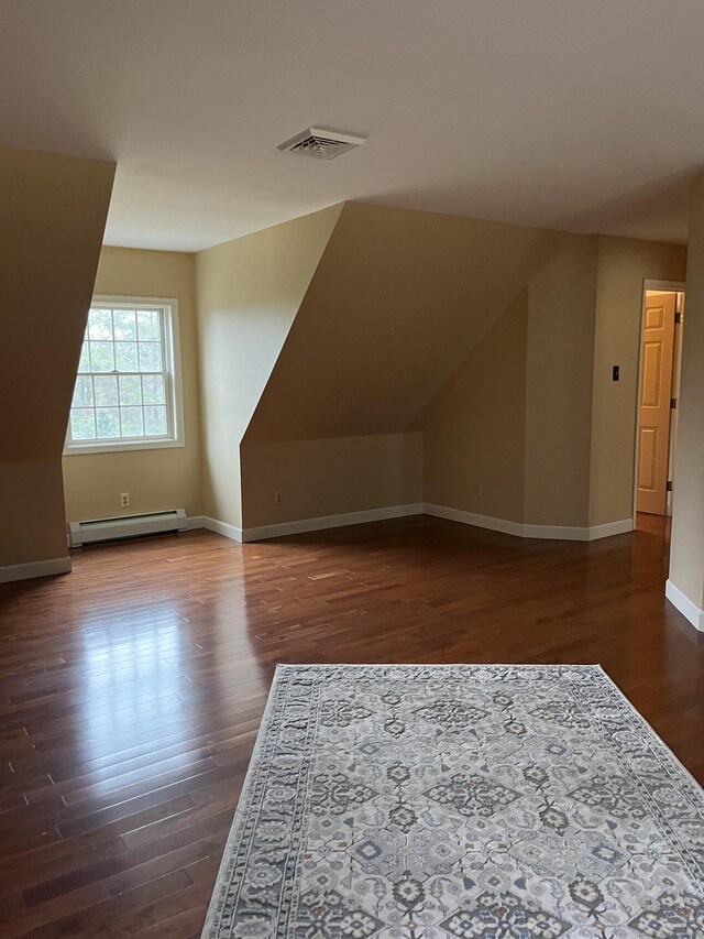 additional living space featuring vaulted ceiling, dark wood-style floors, baseboards, visible vents, and a baseboard heating unit