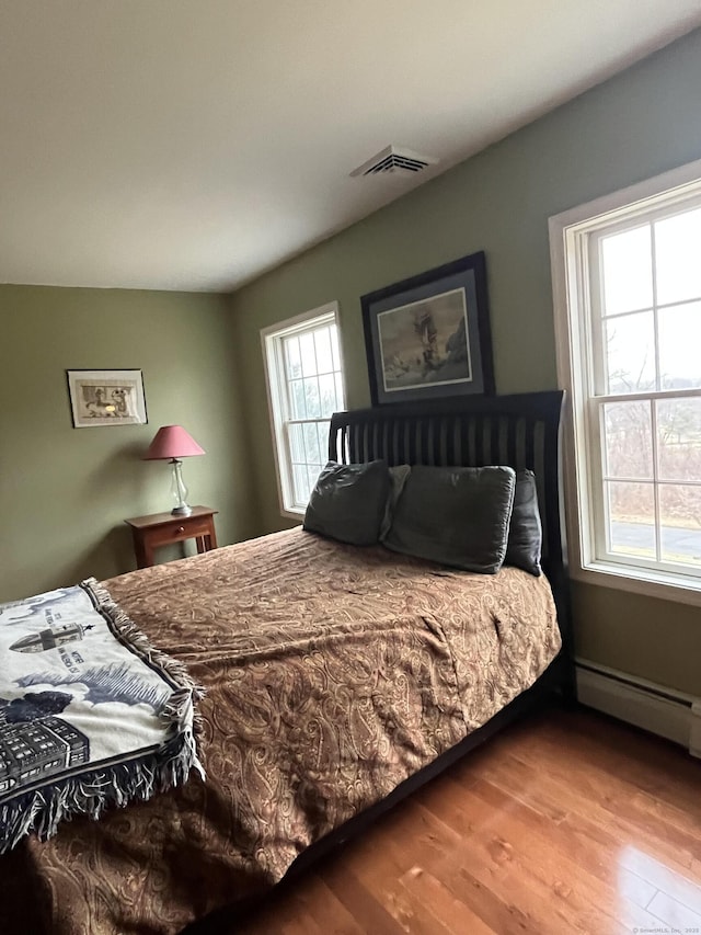 bedroom featuring visible vents, baseboard heating, and wood finished floors