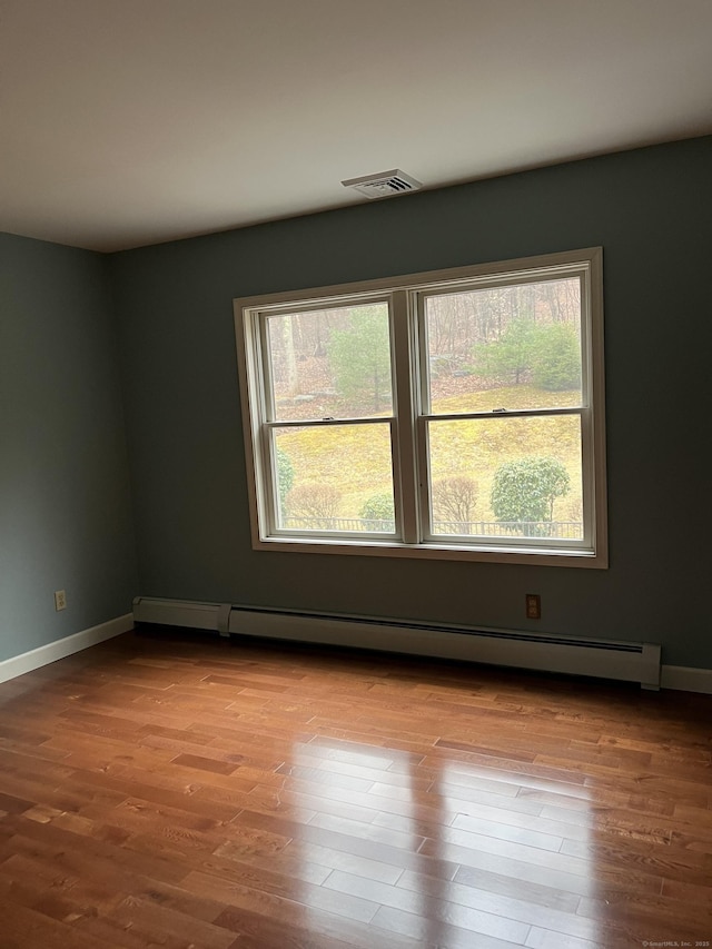 unfurnished room featuring baseboards, visible vents, wood finished floors, and a baseboard heating unit