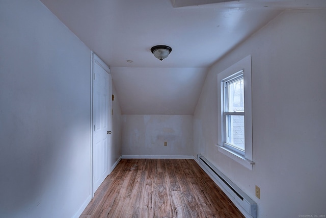 additional living space with vaulted ceiling, a baseboard heating unit, and light wood-type flooring