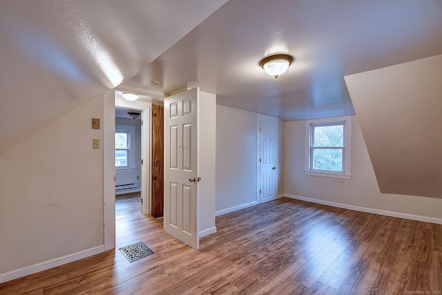 additional living space featuring lofted ceiling, light hardwood / wood-style flooring, and a baseboard radiator