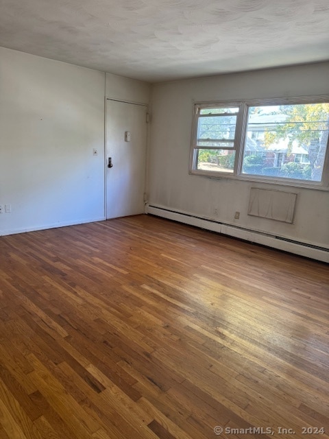 empty room featuring a textured ceiling, baseboard heating, and wood-type flooring