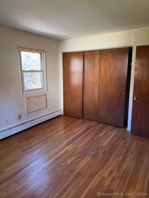 unfurnished bedroom featuring a baseboard heating unit, dark hardwood / wood-style floors, and a closet