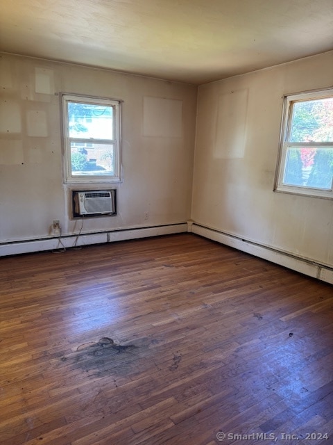 spare room featuring a wall unit AC, dark hardwood / wood-style floors, and a wealth of natural light