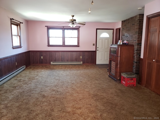 interior space featuring a baseboard heating unit, ceiling fan, wooden walls, and a wealth of natural light