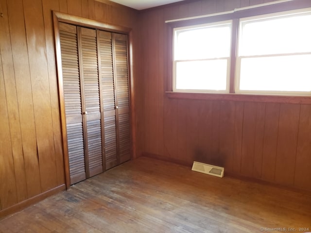 unfurnished bedroom with a closet, hardwood / wood-style flooring, and wooden walls