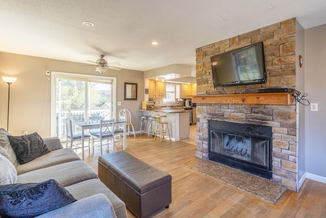 living room with a fireplace, a textured ceiling, light hardwood / wood-style floors, and ceiling fan