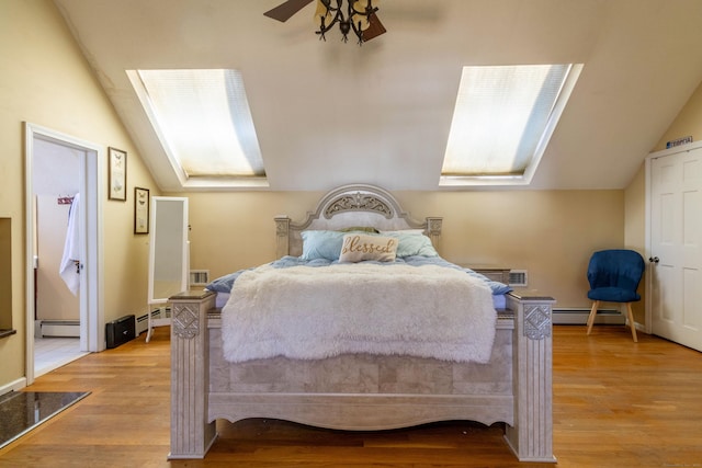 bedroom with a baseboard radiator, light hardwood / wood-style flooring, ceiling fan, and vaulted ceiling with skylight