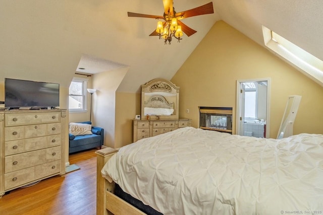 bedroom featuring light wood-type flooring, connected bathroom, lofted ceiling with skylight, and ceiling fan