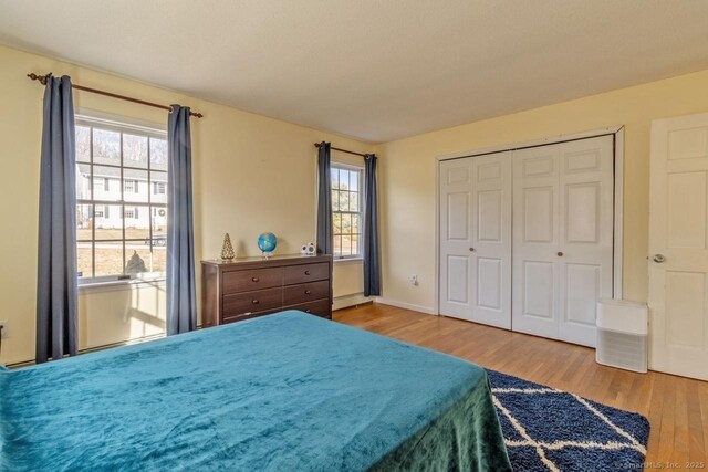 bedroom featuring hardwood / wood-style flooring, multiple windows, a baseboard radiator, and a closet