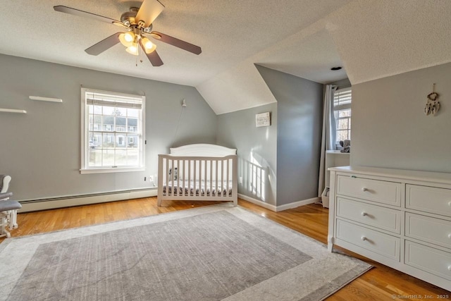 unfurnished bedroom with vaulted ceiling, baseboard heating, ceiling fan, a crib, and light hardwood / wood-style floors