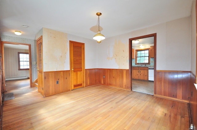 spare room with a baseboard heating unit, wallpapered walls, a wealth of natural light, and wainscoting