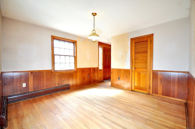 empty room featuring a wainscoted wall, baseboard heating, and wood finished floors