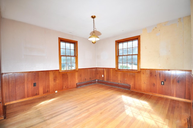 spare room featuring a baseboard radiator, wood finished floors, wainscoting, and wood walls