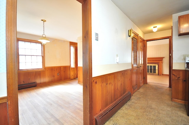 hallway with light wood-type flooring, baseboard heating, wood walls, and wainscoting