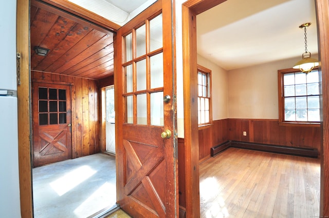 doorway featuring wood walls, wood ceiling, baseboard heating, wainscoting, and wood finished floors