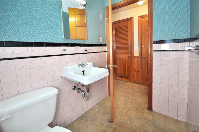 bathroom with a sink, toilet, wainscoting, and wallpapered walls