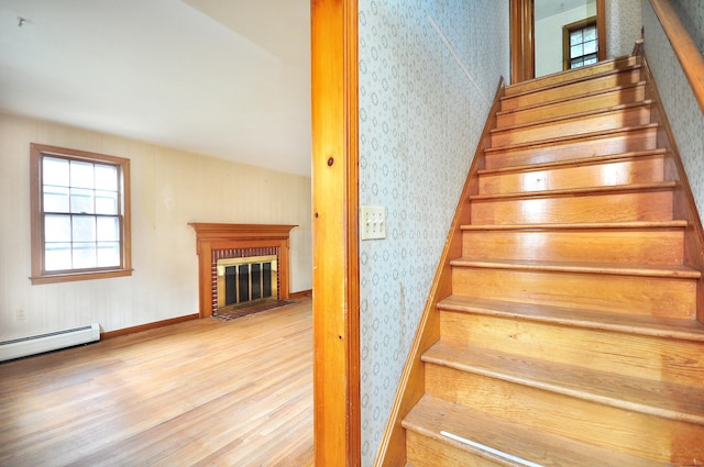 stairs with a baseboard heating unit, wood finished floors, a fireplace, and wallpapered walls