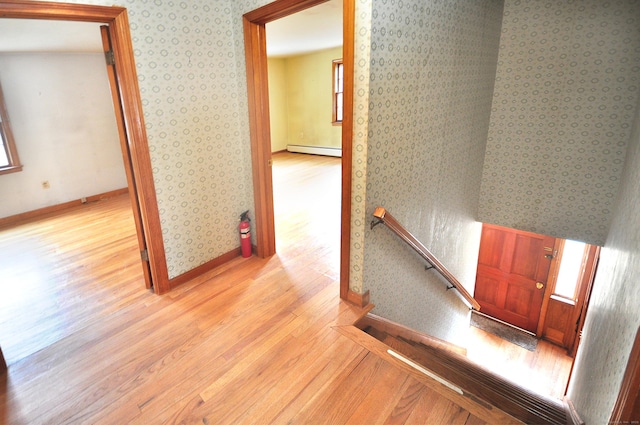 corridor featuring wood finished floors, baseboards, wallpapered walls, an upstairs landing, and baseboard heating