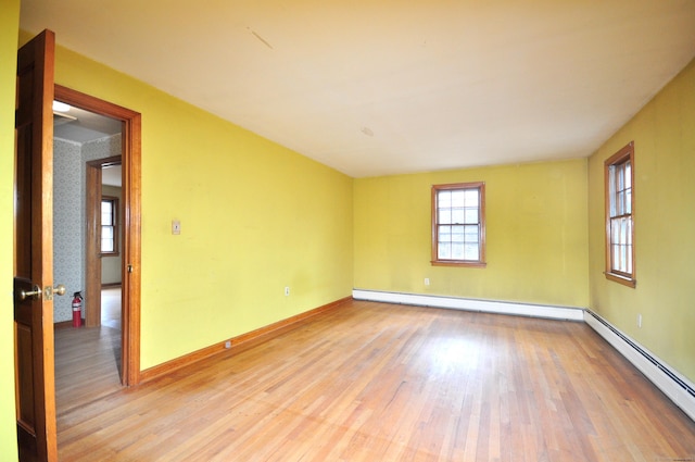 empty room with a baseboard heating unit, baseboards, baseboard heating, and light wood finished floors