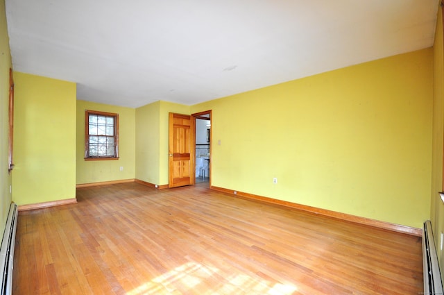 unfurnished room featuring a baseboard heating unit, baseboards, and light wood finished floors