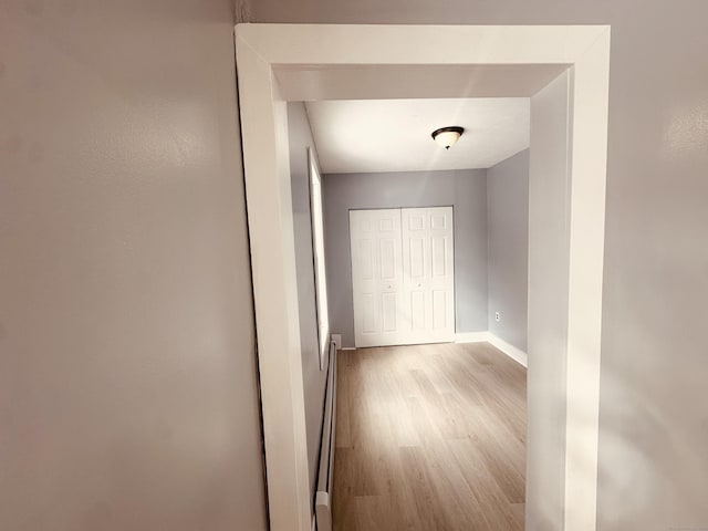 hall featuring light wood finished floors, a baseboard radiator, and baseboards