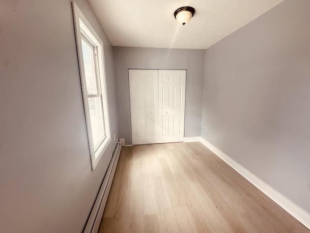 unfurnished bedroom with light wood finished floors, a closet, a baseboard radiator, and baseboards