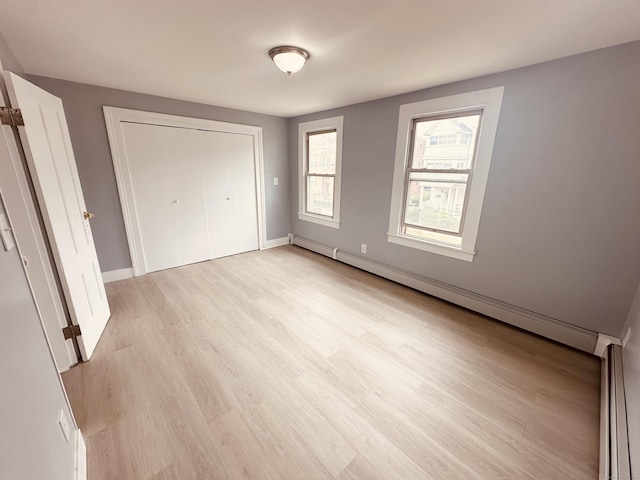 unfurnished bedroom featuring a baseboard radiator, a closet, baseboard heating, light wood-style floors, and baseboards