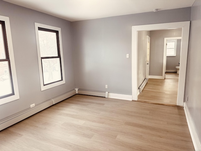 unfurnished room with a baseboard heating unit, light wood finished floors, and baseboards