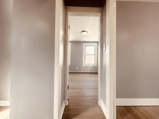 hallway featuring baseboard heating, baseboards, and light wood finished floors