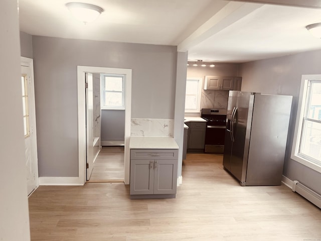 kitchen featuring light wood finished floors, gray cabinets, light countertops, baseboard heating, and appliances with stainless steel finishes