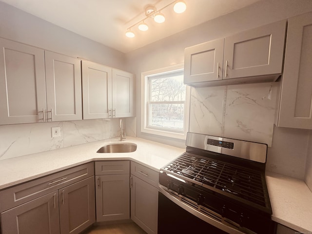 kitchen with light countertops, backsplash, gray cabinetry, stainless steel gas stove, and a sink