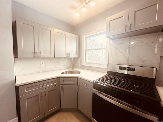 kitchen featuring stainless steel range with gas cooktop, tasteful backsplash, gray cabinets, light countertops, and a sink