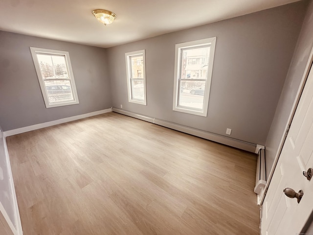 empty room with a baseboard heating unit, light wood-type flooring, and baseboards