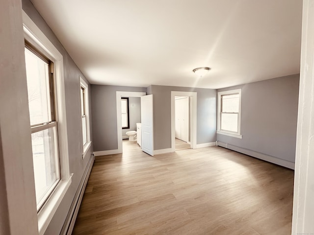 unfurnished room featuring a baseboard heating unit, light wood-type flooring, and baseboards