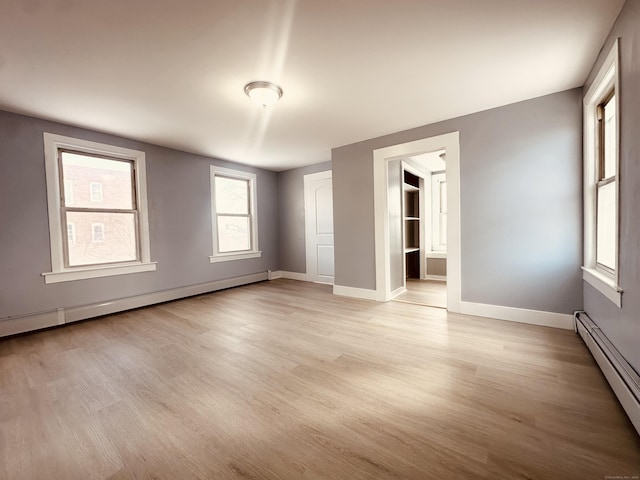 empty room with a baseboard heating unit, baseboards, light wood-style flooring, and baseboard heating