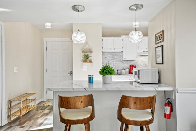 kitchen with white cabinets, a breakfast bar area, light stone countertops, light hardwood / wood-style flooring, and decorative light fixtures