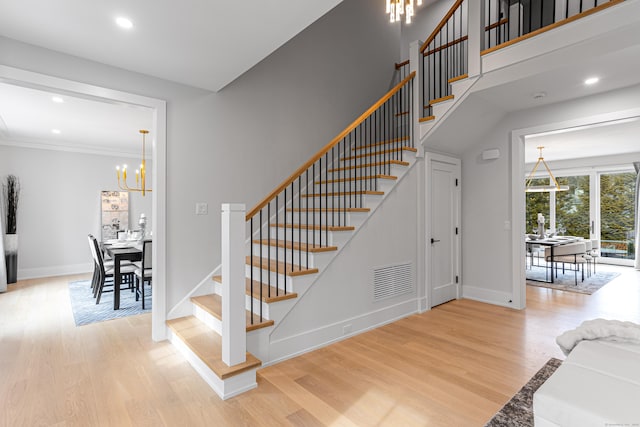 staircase featuring an inviting chandelier, wood-type flooring, and ornamental molding