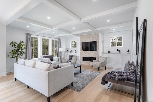 living room featuring coffered ceiling, light hardwood / wood-style floors, a premium fireplace, and beamed ceiling