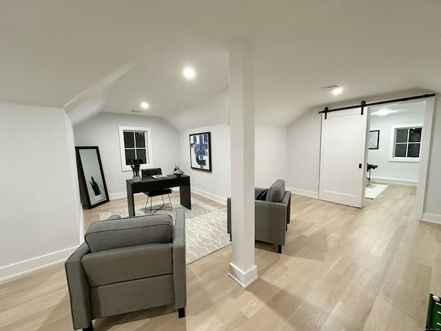 home office featuring lofted ceiling, a barn door, and light hardwood / wood-style floors