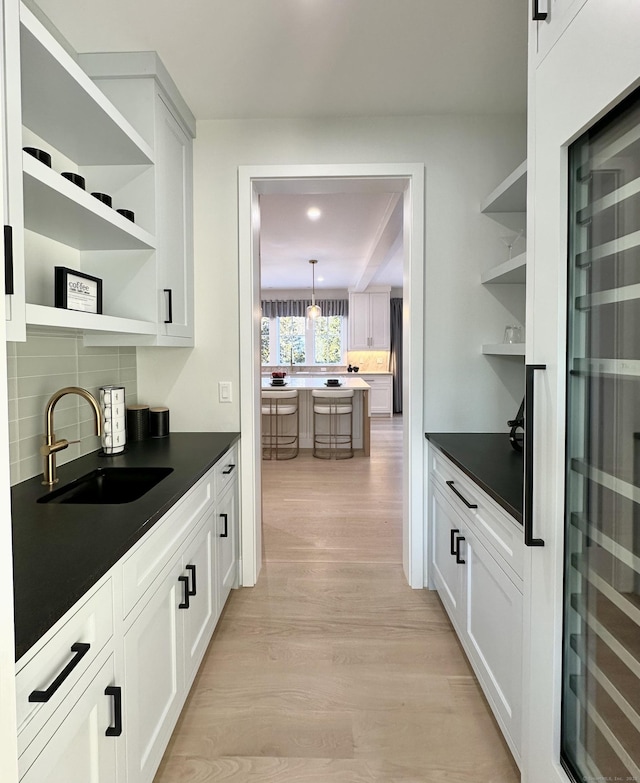 bar featuring tasteful backsplash, white cabinetry, sink, hanging light fixtures, and light wood-type flooring