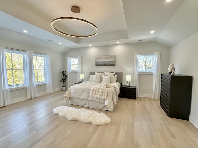 bedroom with multiple windows, lofted ceiling, a raised ceiling, and light wood-type flooring