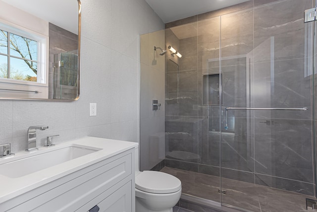 bathroom with vanity, toilet, a shower with door, and tile walls