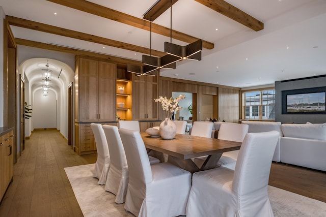 dining room with beamed ceiling, an inviting chandelier, light wood-type flooring, and wood walls