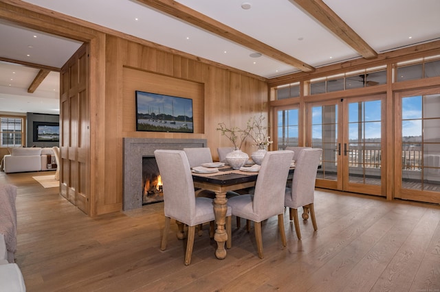 dining space with beamed ceiling, wood-type flooring, a fireplace, and french doors