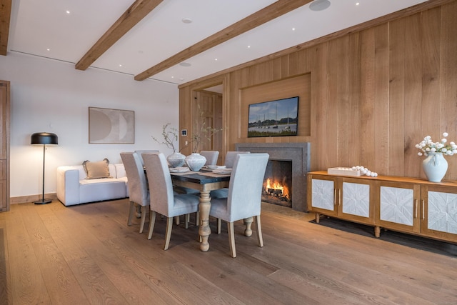 dining room featuring beam ceiling, light hardwood / wood-style floors, and wood walls