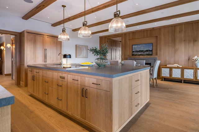 kitchen with pendant lighting, wooden walls, beamed ceiling, an island with sink, and light hardwood / wood-style flooring